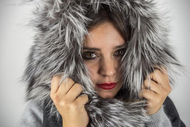 A close-up shot of a puffer jacket showcasing its detailed stitching and high-quality insulation. The jacket is a metallic silver color and features a detachable hood with faux fur trim.