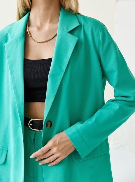 A close-up shot of a woman's torso, showcasing a pastel mint green blouse tucked into high-waisted white trousers. The focus is on the color combination and the texture of the fabrics, emphasizing the fresh and clean aesthetic of the outfit.