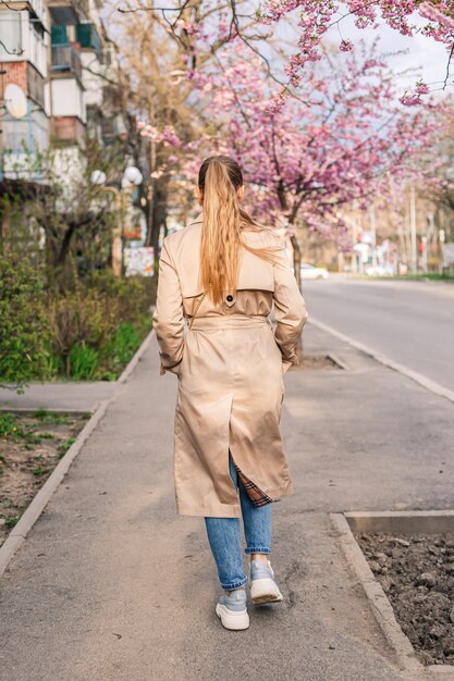 A woman walking down a city street, wearing a pastel peach trench coat over a navy dress and heeled boots. The image highlights the elegance and sophistication of incorporating pastel outerwear into a polished, everyday outfit.