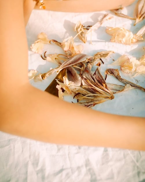 A close-up shot of a person accessorizing a midi slip dress with delicate gold jewelry, including layered necklaces and hoop earrings. The focus is on the accessories and how they elevate the dress from a casual daytime look to a more sophisticated evening style.