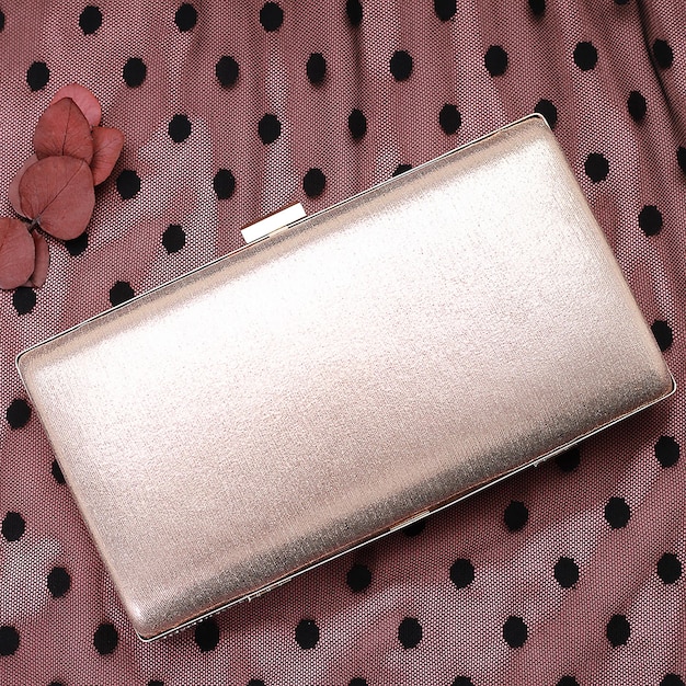 A close-up shot of a stylish clutch bag in a metallic color, with a delicate chain strap. The clutch is adorned with subtle embellishments. The focus is on the texture and detailing of the clutch, highlighting its ability to elevate a nighttime outfit.