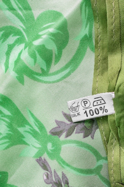 A close-up shot of various clothing labels showing different eco-friendly certifications such as GOTS (Global Organic Textile Standard), Oeko-Tex, and recycled content symbols. The labels are attached to fabrics with textures suggestive of sustainable materials like organic cotton and recycled polyester.