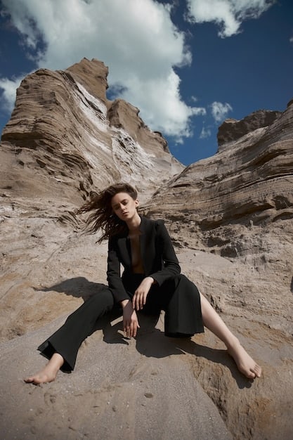 A fashion shoot featuring models in an outdoor, arid landscape. One model is wearing a full terracotta-colored linen ensemble, layered with different textured pieces in slightly varying shades of brown and orange, creating a harmonious, earthy look.